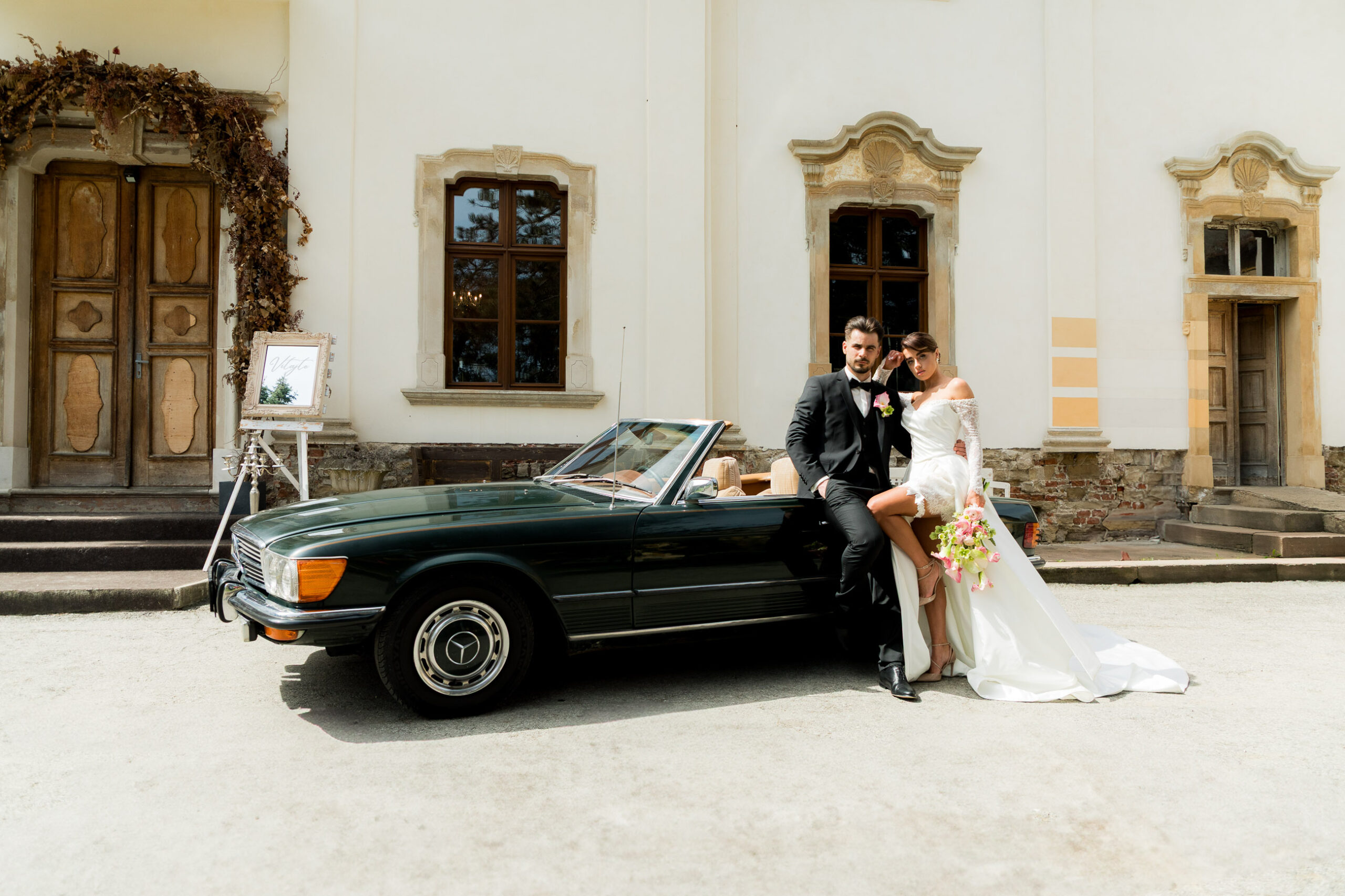 Nevesta a ženích v štýle Old Money pri zelenom veteráne Mercedes-Benz pred Kaštieľom Petrovany.